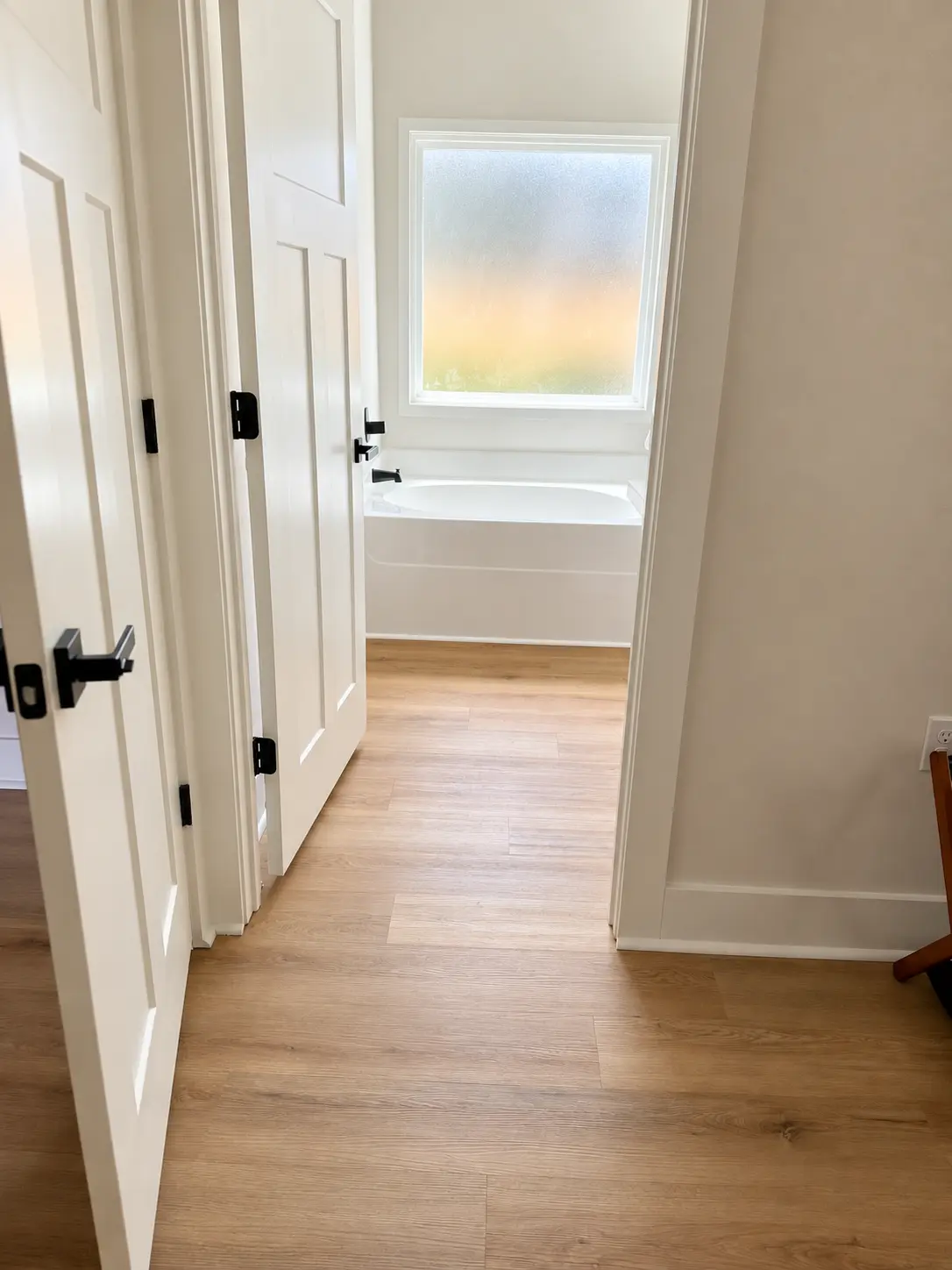 Hallway leading into the primary bath with soaking tub and frosted window